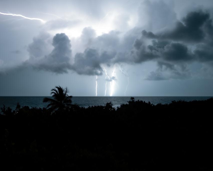 An image of clouds and lighting In the background of a dark Island.